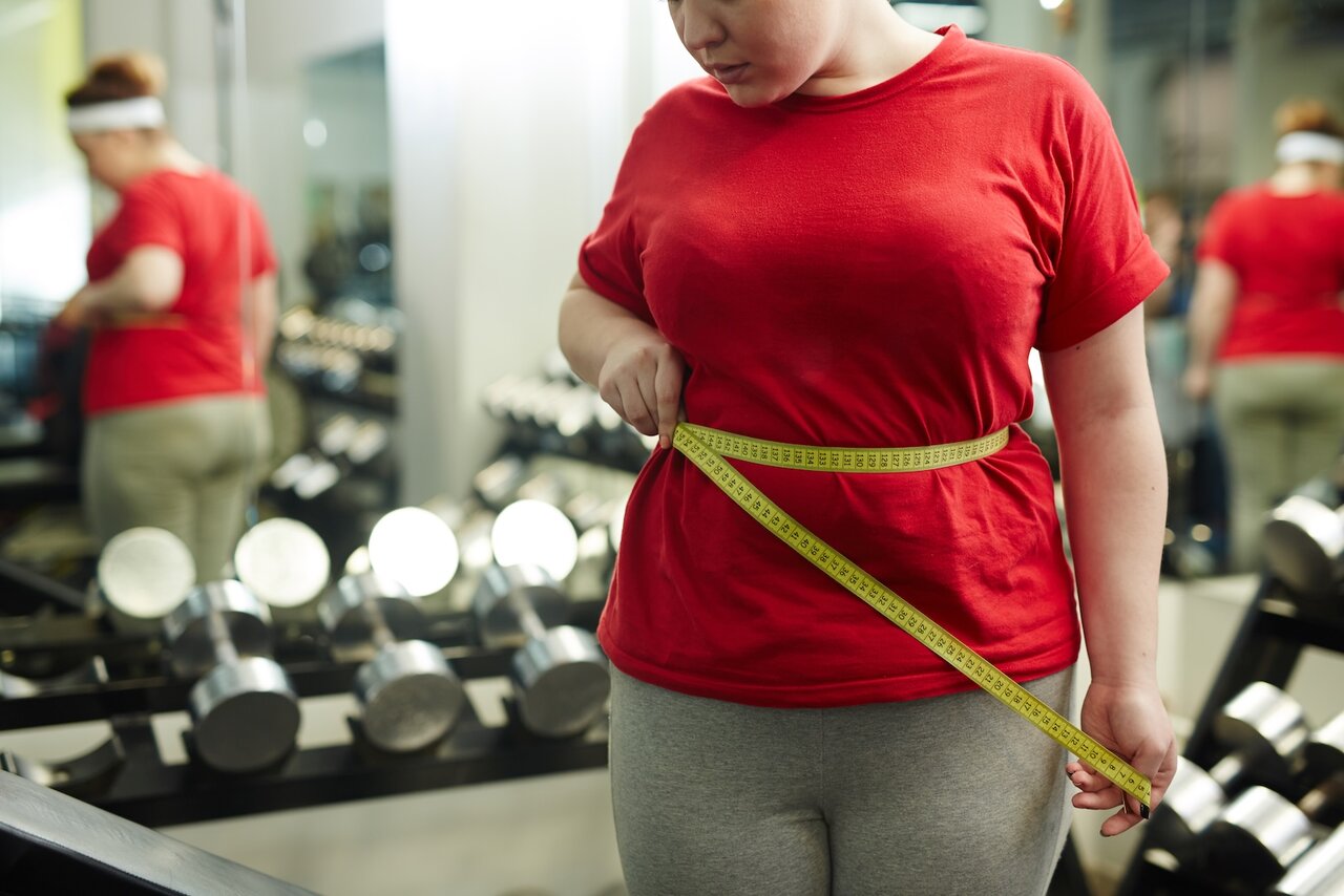 Bild zeigt Übergewichtige Frau misst Taille im Fitnessstudio